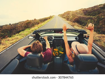 Happy Young Carefree Couple Driving Along Country Road in Convertible at Sunset