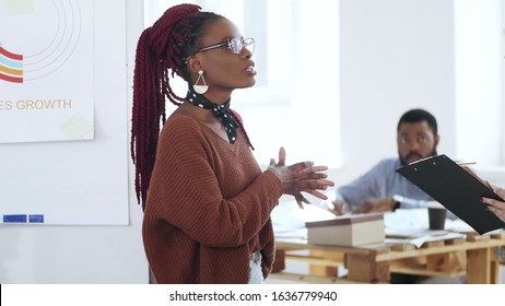 Happy Young Casual African Woman Boss In Eyeglasses Leading Discussion, Chatting To Colleagues At Modern Light Office.