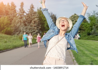 Happy Young Caucasian Bald Woman In Hat And Casual Clothes Enjoying Life After Surviving Breast Cancer. Portrait Of Beautiful Hairless Girl Smiling During Walk At City Park After Curing Disease. 