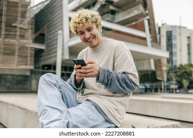 Happy young caucasian blonde man chatting on his phone and smiling at camera. Curly guy wearing on casual clothes on street. Concept technologies. - Powered by Shutterstock