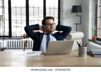 Happy Young Caucasian Businessman In Suit Sit At Office Desk Distracted From Computer Work Dreaming Or Pondering. Smiling Male CEO Look In Window Distance Make Plans. Business Vision Concept.