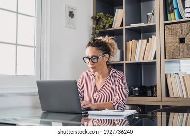 Happy young caucasian businesswoman smiling working online watching webinar podcast on laptop and learning education course conference calling make notes sit at work desk, elearning concept