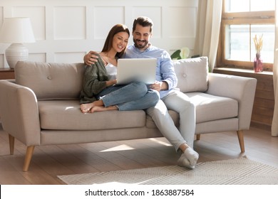 Happy young Caucasian couple renters relax on sofa in living room watch video on laptop together. Smiling man and woman tenants rest on comfortable couch at home use modern computer gadget. - Powered by Shutterstock