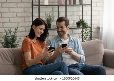 Happy young Caucasian couple sit relax on sofa at home use smartphones gadgets together, smiling millennial man and woman rest on couch in living room have fun browsing cellphone, technology concept - Shutterstock ID 1800910645