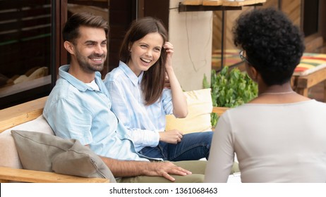 Happy young caucasian couple sitting on couch planning wedding listening to african counselor psychologist insurer planner consulting satisfied family clients talking laughing at meeting