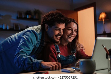 Happy young caucasian couple smiling and having fun watching streaming videos on social media together using a laptop computerwith wireless connection sitting at home at late night. Internet concept - Powered by Shutterstock