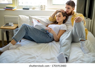 happy young caucasian couple spend weekends together at home. leisure time of married couple, lie on bed and read book or magazine. happy harmonious relationships - Powered by Shutterstock