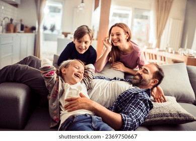 Happy young caucasian family being playful and having fun together on the couch in the living room at home - Powered by Shutterstock