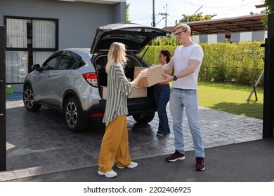 Happy Young Caucasian Family Carry Boxes From Car And Entering New House Together