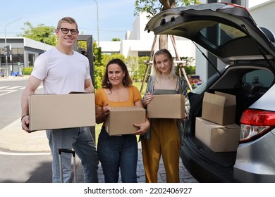 Happy Young Caucasian Family Carry Boxes From Car And Entering New House Together