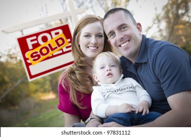 Happy Young Caucasian Family In Front Of Sold Real Estate Sign.