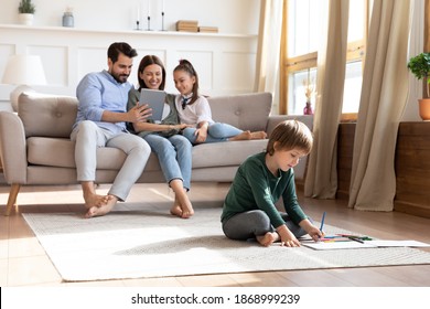 Happy young Caucasian family relax in new cozy design house weekend  use modern table  little boy son drawing  Overjoyed parents rest in own home enjoy time together and small kids children 