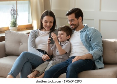 Happy young Caucasian family with small 7s son relax on sofa in living room use modern smartphone together. Smiling parents with little boy child talk on video call on cellphone. Technology concept.