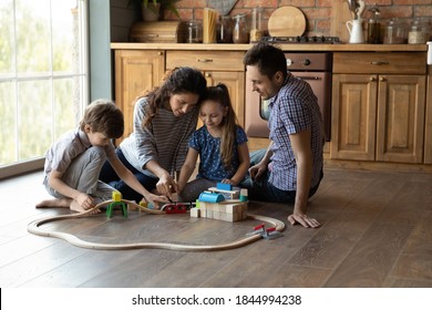 Feliz familia joven caucásica con dos niños pequeños sentados en el piso en la cocina jugando juntos juguetes. Amantes de cuidar a los padres se divierten y juegan en actividades de juegos con niños pequeños en casa.