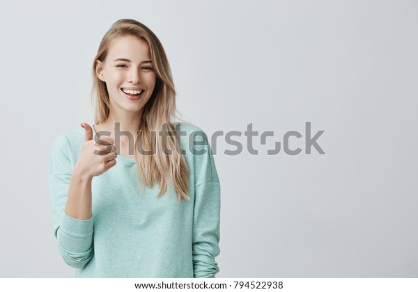 青い袖の長いシャツを着た幸せな白人の女性が親指サインを作り 陽気に微笑み 誰かに対する支えと尊敬を示す 本文の言語 私はそれが好きです お疲れさまでした の写真素材 今すぐ編集