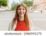 Happy young caucasian girl smiling at camera standing at city street. Outside portrait of joyful beautiful italian woman over urban background.