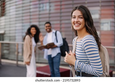 Happy Young Caucasian Girl Smiling Looking At Camera Standing On Blurred Background Of Her Classmates. Students Spend Their Free Time Outdoors. Mood Good, Lifestyle, Concept.