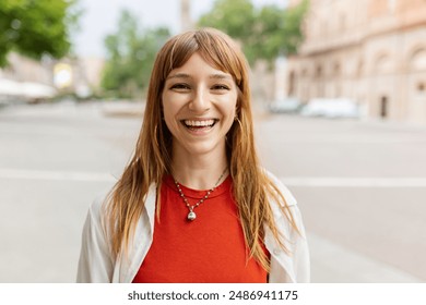 Happy young caucasian girl smiling at camera standing at city street. Outside portrait of joyful beautiful italian woman over urban background.