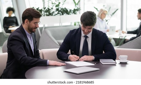 Happy young Caucasian male employee put signature document close deal and employer boss in office  Young businessmen partners sign contract paperwork make business agreement at meeting 