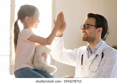 Happy Young Caucasian Male Pediatrician Give High Five To Small Kid Patient In Private Hospital. Smiling Man Doctor Or GP Make Deal With Little Girl Child In Clinic. Pediatric, Healthcare Concept.