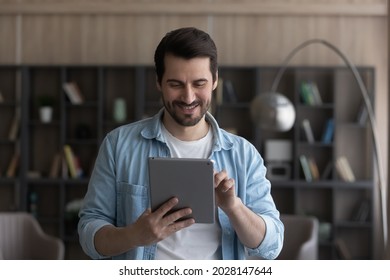 Happy young caucasian man holding digital computer tablet in hands, enjoying web surfing information, communicating distantly in social network, playing online games or using software applications. - Powered by Shutterstock