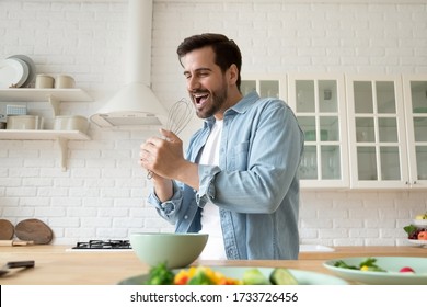 Happy young Caucasian man preparing food in modern design kitchen have fun singing and dancing, overjoyed millennial guy cooking breakfast at home enjoy leisure domestic weekend in new apartment