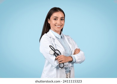 Happy young caucasian medical doctor wears a lab coat and stethoscope, standing with confidence against a soothing blue background - Powered by Shutterstock