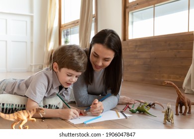 Happy young Caucasian mom   small 6s son lying floor at home have fun drawing together in album  Smiling loving mother nanny involved in creative activity painting  Hobby concept 