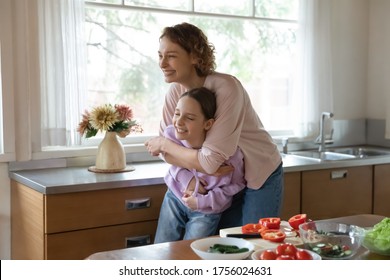 Happy young Caucasian mom and teen daughter have fun laugh cooking together at home kitchen, overjoyed mother and teenage daughter feel crazy playful preparing food together, family concept