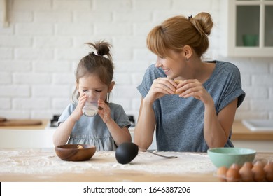 Happy young Caucasian mother and little preschooler daughter sit at kitchen table baking eating cookies together, smiling mom have fun with small girl child teach bakery enjoy family weekend at home