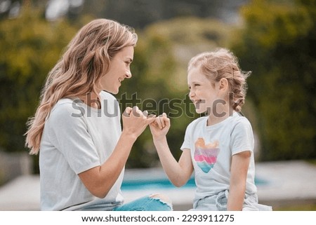 Happy young caucasian mother sitting with her adorable little daughter in the garden at home and making pinky promises. Cute little girl bonding with her parent in the backyard swearing to secrecy