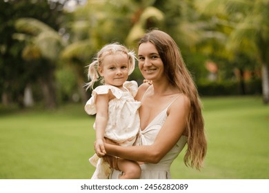 Happy young caucasian mother and toddler girl daughter look at the camera and smiling, summer park on background - Powered by Shutterstock