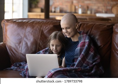 Fröhliche junge kaukasische Mutter und kleine Tochter entspannen sich zu Hause auf dem Sofa und schauen Video auf Laptop, lächeln optimistische kranke Krebspatientin Mutter und kleine Mädchen auf Couch mit Computer ruhen