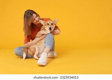 Happy young caucasian woman holding a dog corgi, sitting on yellow studio background and embracing her pet, copy space, banner - Powered by Shutterstock