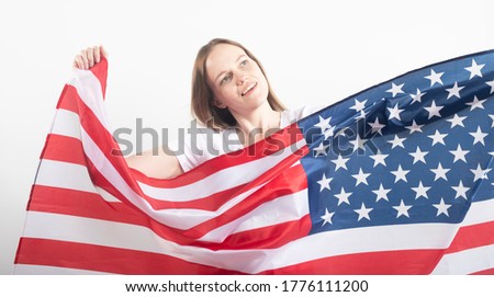 Happy young caucasian woman holding large American US flag over white background