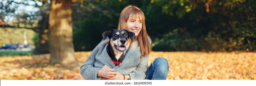 Happy young Caucasian woman hugging dog in park. Owner with pet on autumn fall day. Best friends having fun outdoor. Friendship of human with domestic animal. Web banner header.
