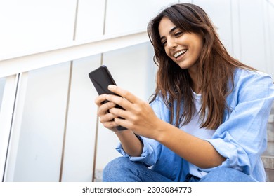 Happy young caucasian woman looking mobile phone sitting on stairs in street. Copy space.