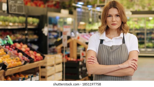 Happy Young Caucasian Woman Manager In Apron Standing In Supermarket Indoors And Looking At Camera. Female Beautiful Worker At Grocery Store. Close Up Portrait Concept. Retail Business