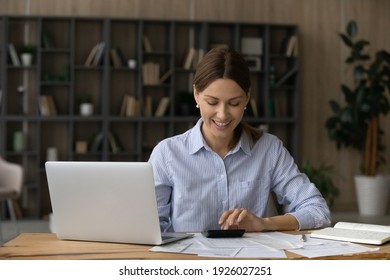 Happy young Caucasian woman sit at desk manage budget use machine paying online on computer. Smiling female calculate expenses expenditures on calculator, care of finances. Saving concept.