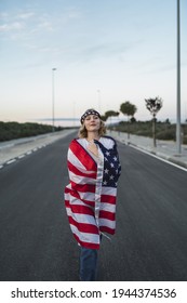 A Happy Young Caucasian Woman Wearing A Bandana And Holding A US Flag While Walking On The Road