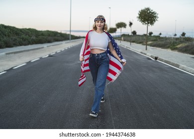 A Happy Young Caucasian Woman Wearing A Bandana And Holding A US Flag While Walking On The Road