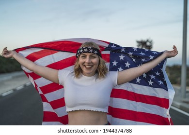 A Happy Young Caucasian Woman Wearing A Bandana And Holding A US Flag While Walking On The Road