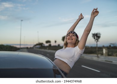 A Happy Young Caucasian Woman Wearing A Bandana With US Flag Print While Leaning Out Of Car Window