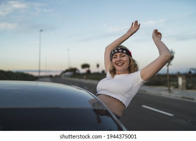 A Happy Young Caucasian Woman Wearing A Bandana With US Flag Print While Leaning Out Of Car Window