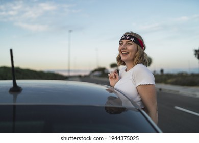 A Happy Young Caucasian Woman Wearing A Bandana With US Flag Print While Leaning Out Of Car Window