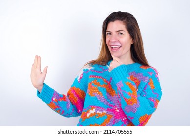 Happy Young Caucasian Woman Wearing Vintage Colorful Sweater Over White Background Sings Favourite Song Keeps Hand Near Mouth As If Microphone Wears Wireless Headphones, Listens Music