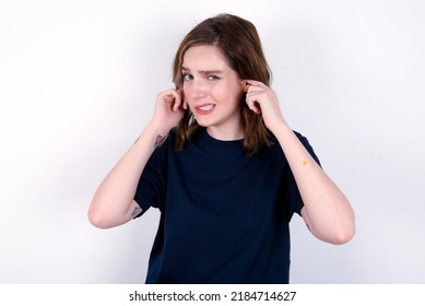 Happy Young Caucasian Woman Wearing Black T-shirt Over White Background Ignores Loud Music And Plugs Ears With Fingers Asks To Turn Off Sound