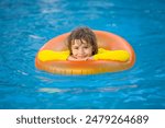 Happy young child enjoying summer vacation outdoors in water in the swimming pool. Cute little kid in swimming suit swim on an inflatable ring. Kid floating in a pool.