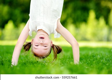 Happy young child playing head over heels on green grass in spring park 