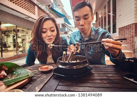 Happy young chinese couple sitting at cafe outside enjoying traditional asian food. Widescreen shooting.